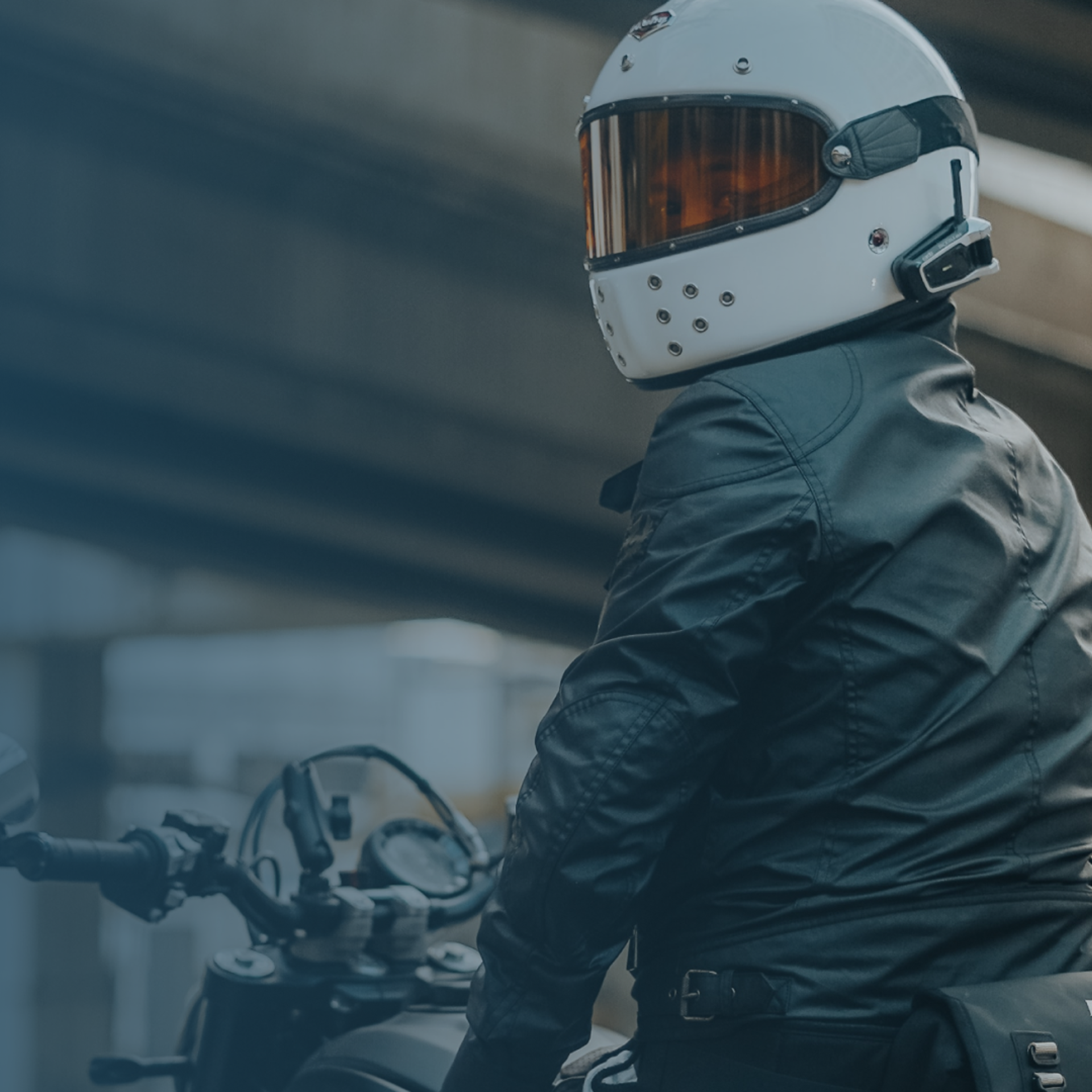 Billede af en motorcyklist med en sort læderjakke på og en hvid hjelm, som kigger sig over skulderen 